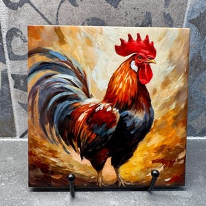 May include: A vibrant painting of a rooster with a red comb and wattle, and a colorful plumage of red, blue, and black. The artwork is displayed on a square tile, showcasing a rustic, farm-inspired theme.