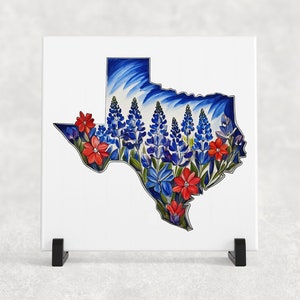 May include: A white ceramic tile with a blue and white outline of the state of Texas. The outline is filled with bluebonnet flowers and red wildflowers.
