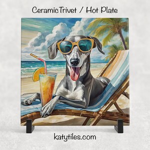 May include: Ceramic trivet featuring a grey and white dog wearing sunglasses, relaxing on a beach chair with a tropical drink. The background shows a beach scene with palm trees and ocean waves. The text "katytiles.com" is visible.
