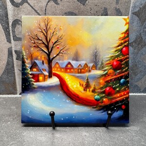 Puede incluir: Una escena de invierno con un camino nevado que lleva a un pueblo de casas con ventanas brillantes. Un gran árbol de Navidad con adornos coloridos está en primer plano.