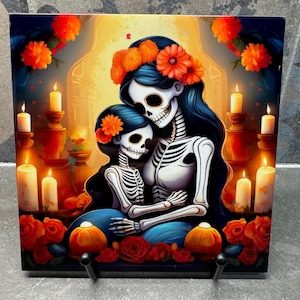 May include: A square ceramic tile featuring a Day of the Dead theme. It depicts two skeleton figures embracing, adorned with floral crowns and surrounded by candles and roses. The color palette includes blue, orange, red, and white.