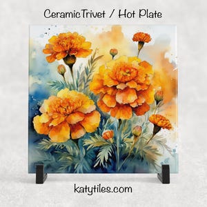 Puede incluir: Salvamanteles de cerámica cuadrado con una pintura de acuarela de flores de caléndula naranja. Las flores tienen pétalos detallados sobre un fondo azul y amarillo. El texto "Ceramic Trivet / Hot Plate" está en la parte superior.
