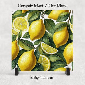 May include: Ceramic trivet or hot plate featuring a vibrant lemon design. The square trivet showcases bright yellow lemons and green leaves against a white background. The text "Ceramic Trivet / Hot Plate" and "katytiles.com" are visible.