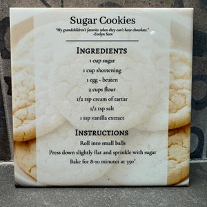 Puede incluir: Una baldosa de cerámica blanca con una receta de galletas de azúcar. La receta incluye ingredientes como azúcar, manteca vegetal, harina y extracto de vainilla. Las instrucciones son enrollar la masa en bolas, presionarlas hasta que queden planas y hornear a 350 grados Fahrenheit durante 8-10 minutos.