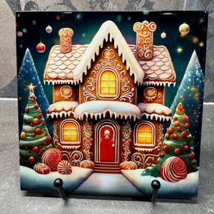 May include: A gingerbread house with white frosting and candy cane accents sits in a snowy winter scene. The house has lit windows and a red door. Two Christmas trees with red ornaments stand on either side of the house.