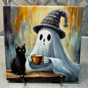 Könnte beinhalten: Ein weißer Geist, der einen schwarzen Hexenhut trägt, sitzt an einem Tisch mit einer schwarzen Katze. Der Geist hält eine braune Tasse. Der Hintergrund ist ein farbenfrohes abstraktes Gemälde.