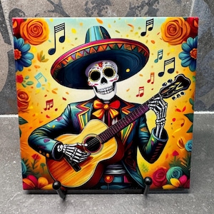 May include: A colorful square tile featuring a skeleton in a sombrero playing a guitar. The skeleton wears a decorated suit and bow tie, surrounded by musical notes and floral accents in a vibrant, Day of the Dead theme.
