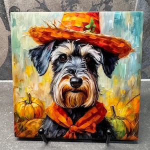 May include: Square ceramic tile featuring a Schnauzer dog wearing an orange scarf and a straw hat. The dog is surrounded by pumpkins in a colorful, impressionistic style. The artwork has a fall theme.