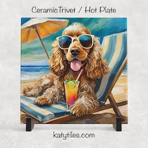 May include: Ceramic trivet featuring a Cocker Spaniel wearing sunglasses, relaxing on a beach chair under an umbrella. The dog is holding a tropical drink. The background shows a beach scene with blue water and sky. Text reads "Ceramic Trivet / Hot Plate" and "katytiles.com".