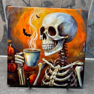 May include: A painted ceramic tile featuring a skeleton holding a steaming cup of coffee. The background is a vibrant orange with bats flying in the sky. Pumpkins are scattered around the base of the tile.