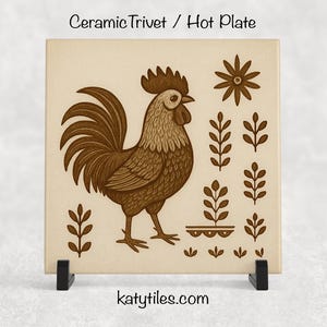 May include: A square ceramic trivet or hot plate with a brown rooster illustration and floral accents. The trivet has the text "Ceramic Trivet / Hot Plate" at the top and "katytiles.com" at the bottom. The trivet is displayed on a black stand.