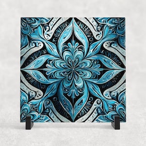 Könnte beinhalten: Eine quadratische Glasfliese mit einem blauen und schwarzen Mandala-Design. Das Mandala zeigt komplizierte florale Muster und Wirbel. Die Fliese wird auf einem schwarzen Metallständer präsentiert.