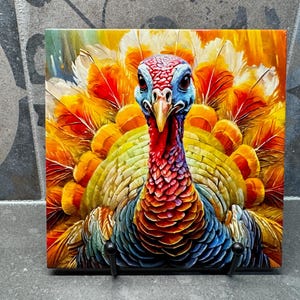 Puede incluir: Azulejo de cerámica cuadrado con una colorida ilustración de un pavo. El pavo tiene la cabeza roja y azul, con un pico amarillo. Sus plumas son una mezcla de amarillo, naranja y rojo. El azulejo está montado sobre un soporte de metal negro.