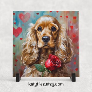 May include: A painting of a brown and white cocker spaniel dog with a red rose in its mouth. The dog is surrounded by red hearts on a blue and green background. The painting is on a tile with a black stand.