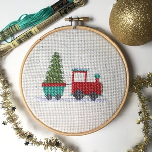 Pode incluir: Um padr&atilde;o de ponto cruz de um trem de brinquedo vermelho puxando um vag&atilde;o verde com uma &aacute;rvore de Natal dentro. O trem e o vag&atilde;o est&atilde;o em um fundo branco com um efeito de neve azul claro.