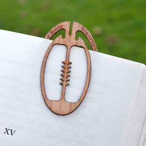 Peut inclure: Un marque-page en bois en forme de ballon de rugby. Le marque-page porte les mots "Le Stade" et "Bleu Rouge".