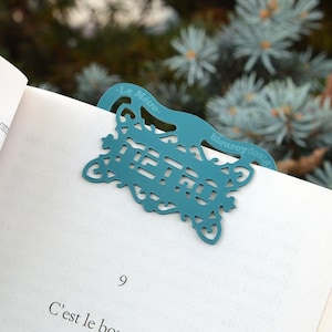 Può includere: Un segnalibro in metallo blu turchese con un design decorativo e il testo "Le Métro" e "blenroydesign".