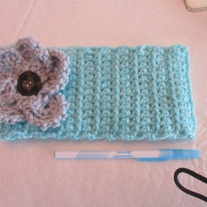 May include: A light blue crocheted headband with a grey crocheted flower and a black button in the centre.