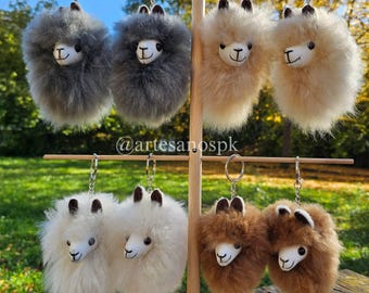 Puede incluir: Un conjunto de diez llaveros de alpaca esponjosos en varios colores, incluyendo gris, marrón y blanco. Cada llavero presenta una pequeña alpaca con una cara linda y un anillo plateado para sujetar las llaves.