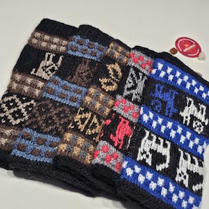 Könnte beinhalten: Ein Stapel von vier gestrickten Beinwärmern mit aufwendigen Mustern. Die Beinwärmer haben eine schwarze Basis mit Designs in Braun, Blau, Rot und Weiß. Die Muster umfassen geometrische Formen und Tierfiguren. Das Etikett lautet "Artesanos".