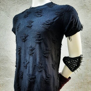 Puede incluir: Camiseta negra con un aspecto desgastado y rasgado. La camiseta tiene un corte holgado y un escote redondo.