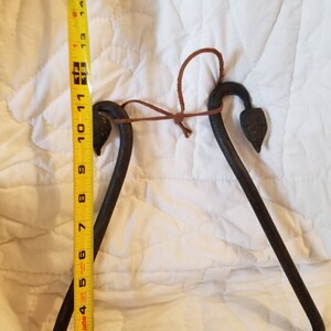 May include: A black metal triangle with rounded corners and a leather strap. The triangle is approximately 10 inches in length.