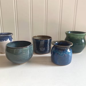 May include: Five handcrafted ceramic pots in various shapes and sizes. The pots feature a range of colours, including blue, green, and white, with unique glaze effects. These decorative pots are ideal for small plants or as home decor.