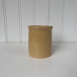 May include: A small, pale yellow ceramic jar with a smooth, rounded surface. The jar is empty and has a simple, classic design.