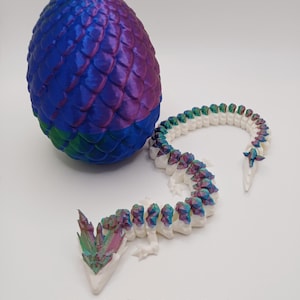 May include: A 3D-printed dragon egg and articulated dragon. The egg is blue, purple, and green with a textured, scaled surface. The dragon is white with triple-color accents. Text on the image reads "White/Triple-Color".