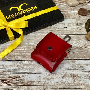 May include: A red leather case with a silver hook and a black button. The case is sitting on a wooden surface with a black gift box with a yellow ribbon and the text "GOLDENHORN expert in handcraft" on it.
