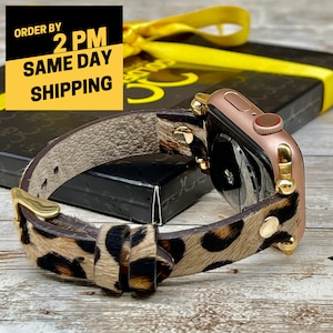 May include: A gold Apple Watch with a leopard print leather band. The watch is on a wooden surface and has a gold buckle.