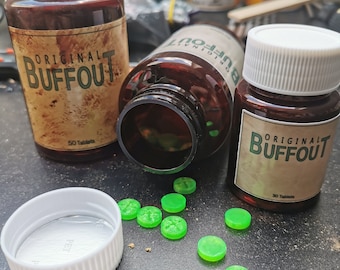 May include: Two brown bottles with white lids and labels that say "Original Buffout" and "50 Tablets".  Green round pills are scattered on a dark surface.  One bottle is lying on its side with the lid off.