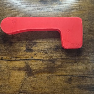 May include: A red plastic handle with a curved shape and a rectangular opening. The handle is designed for use with a door or other object.