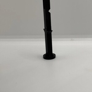May include: A vertical black plastic tool featuring a cylindrical base, a slender central shaft, and a rectangular opening at the top. The object has a small triangular protrusion on the side of the shaft and a flat, circular bottom for stability.