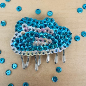May include: A blue and white sequined cloud with a beaded rain design. The cloud is made of iridescent sequins and has a white beaded fringe.