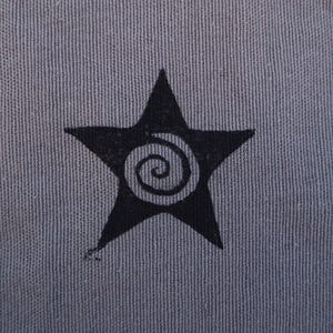 May include: A square, gray fabric patch with a black star design. The star has a spiral design in the center. The edges of the patch are scalloped.