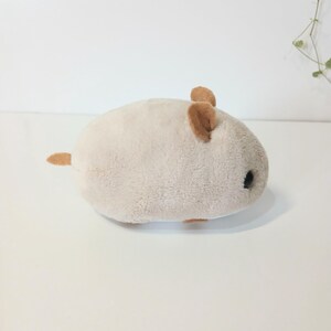 Pu&ograve; includere: Un giocattolo di peluche a forma di criceto beige chiaro con orecchie e coda marroni. Il giocattolo ha un corpo arrotondato e occhi neri, che gli conferiscono un aspetto carino. Realizzato in materiale morbido e soffice.