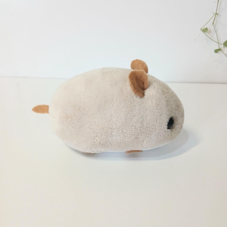 Pu&ograve; includere: Un giocattolo di peluche a forma di criceto beige chiaro con orecchie e coda marroni. Il giocattolo ha un corpo arrotondato e occhi neri, che gli conferiscono un aspetto carino. Realizzato in materiale morbido e soffice.