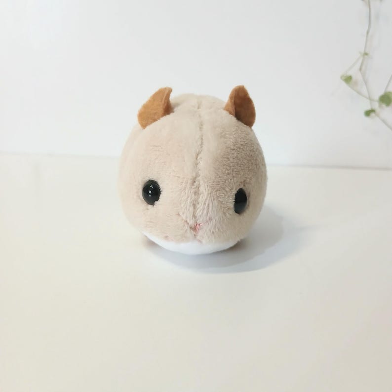 Pu&ograve; includere: Un peluche a forma di criceto di colore beige chiaro, con piccole orecchie marroni e occhi neri. Il giocattolo ha una pancia bianca e un piccolo naso rosa. Il criceto &egrave; rotondo e morbido.