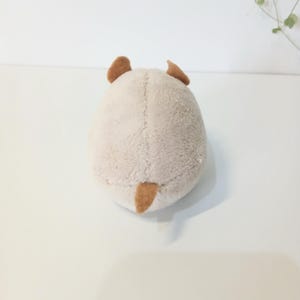 Pu&ograve; includere: Un giocattolo di peluche a forma di piccolo animale, visto da dietro. Il giocattolo &egrave; principalmente beige con orecchie marroni e una piccola coda marrone. Il peluche ha un aspetto morbido e strutturato.