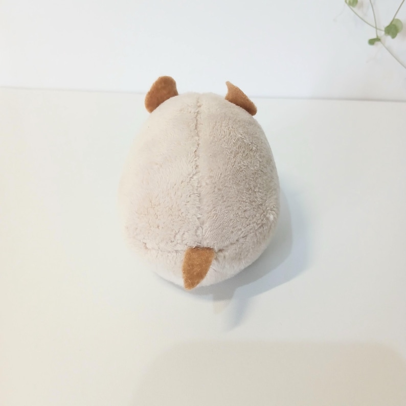 Pu&ograve; includere: Un giocattolo di peluche a forma di piccolo animale, visto da dietro. Il giocattolo &egrave; principalmente beige con orecchie marroni e una piccola coda marrone. Il peluche ha un aspetto morbido e strutturato.