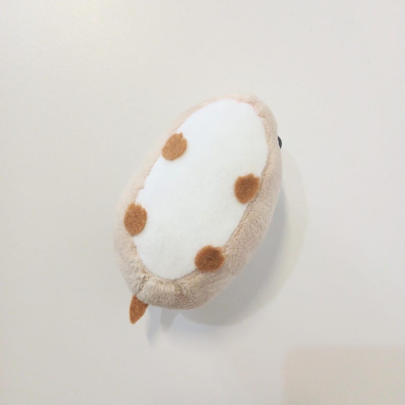 Pu&ograve; includere: Un giocattolo di peluche di forma ovale, nei toni del beige, bianco e marrone. Il giocattolo ha un centro bianco con quattro macchie marroni e un bordo beige. Una piccola coda marrone si estende da un'estremit&agrave;. Il giocattolo &egrave; progettato per assomigliare a un piccolo animale.
