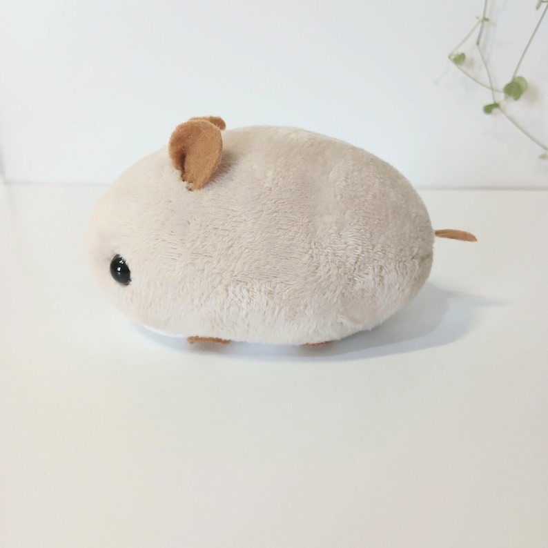 Pu&ograve; includere: Un giocattolo di peluche a forma di criceto di colore beige chiaro, con orecchie marroni e una piccola coda. Il giocattolo ha un corpo rotondo e un occhio nero. Questo giocattolo morbido &egrave; adatto ai bambini.