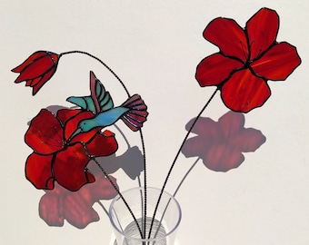 Hummingbird on a bouquet of red azalées in Tiffany stained glass. Decoration of flowers and glass hummingbird for festive table.