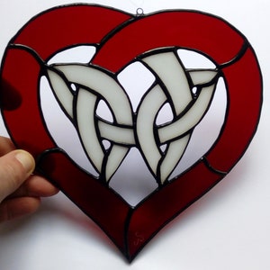Könnte beinhalten: Ein rotes, herzförmiges Bleiglasfenster mit einem weißen keltischen Knotendesign in der Mitte.