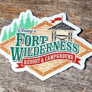 May include: A white sticker with a brown, green, and red design. The sticker features the text "Disney's Fort Wilderness Resort & Campground".