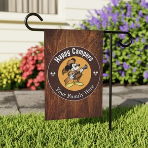 May include: A brown wooden garden flag with a cartoon image of Mickey Mouse dressed as a camper. The flag has a circle with the text "Happy Campers Your Family Here" and two Mickey Mouse ears on either side of the circle.