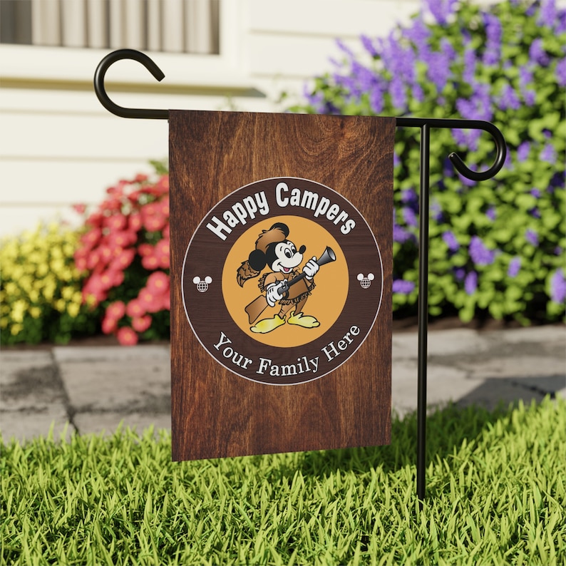 May include: A brown wooden garden flag with a cartoon image of Mickey Mouse dressed as a camper. The flag has a circle with the text "Happy Campers Your Family Here" and two Mickey Mouse ears on either side of the circle.