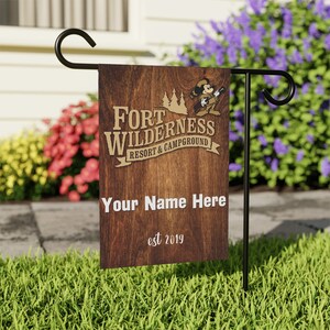 May include: A brown wooden garden flag with a cartoon mouse holding a rifle. The text "Fort Wilderness Resort & Campground" is in gold lettering. The text "Your Name Here" and "est 2019" are also on the flag.