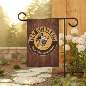 May include: A brown wooden garden flag with a yellow circle featuring a cartoon mouse wearing a cowboy hat and holding a rifle. The text "Fort Wilderness The Williamsons" is inside the circle.